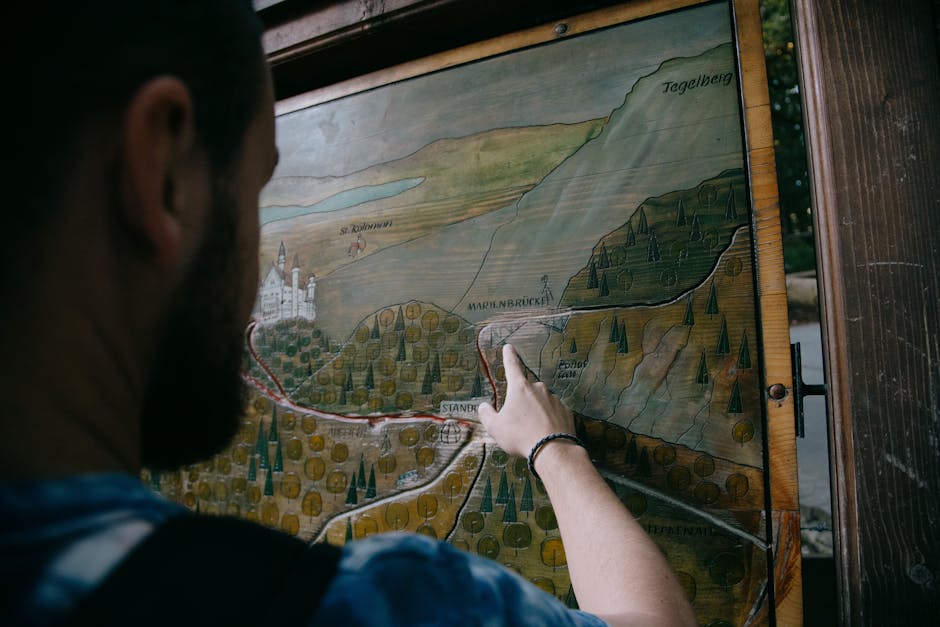 Back view of anonymous man pointing on wooden board with carved painting of mountains and roads