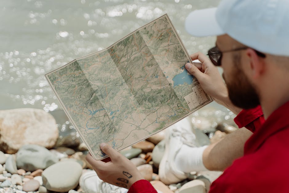 A man studies a map beside a rocky river, focusing on navigation and adventure.